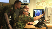 Drei Soldaten arbeiten an einem Computer, zwei sitzen vor den Bildschirmen, einer steht dahinter.