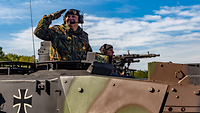Ein Soldat schaut aus einem Panzer heraus und grüßt militärisch.