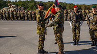 Ein Soldat übergibt auf dem Appellplatz die Truppenfahne an einen Soldaten vor einer Formation.