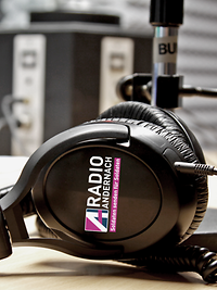 Radio Andernach Kopfhörer Kopfhörer mit dem Radio Andernach Logo im Fokus. Sie liegen auf dem Tisch in einem Tonstudio.