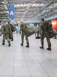 Mehrere Soldaten in Flecktarn Uniformmit Gepäck betreten die Halle eines Flughafens.