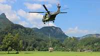 An einem Hubschrauber hängt ein großes Netz mit einem Metallbehälter gefüllt. 