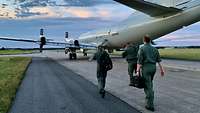 Mehrer Menschen in olivgrünen Overalls gehen auf ein viermotoriges Propellerflugzeug zu.