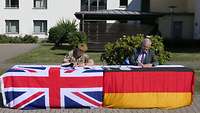 Zwei Männer unterzeichnen ein Papier, ein Mann trägt eine britsche Uniform, der andere einen Anzug.