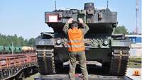 Ein Soldat mit Warnweste weist einen Panzer beim Herunterfahren eines Eisenbahnwaggons ein