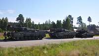 Drei Panzer stehen auf der Straße, im Hintergrund Bäume, im Vordergrund eine Wiese 