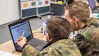 Zwei Soldaten sitzen vor einem Laptop.