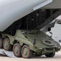 Auf einem Flugfeld parkt ein GTK Boxer rückwärts in den Frachtraum eines A400M ein.