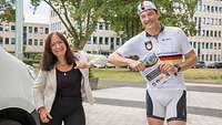 Weibliche Person in zivil und männliche Person in Radfahrer-Kleidung berühren einander an den Ellenbogen 