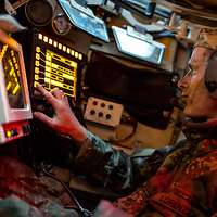 Ein Soldat sitzt mit Kopfhörern in einem Panzer und schaut auf zwei Bildschirme.