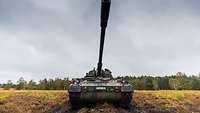 Frontalansicht einer Panzerhaubitze 2000 mit weit ausladendem Geschützrohr, im Hintergrund Wald