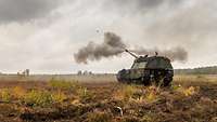Ein Panzer steht auf einem Übungsplatz und schießt. Rauch steigt auf.
