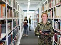 Eine Soldatin posiert für Bildung und Forschung in der Bundeswehr Eine Soldatin steht mit einem Tablet in der Hand in einer Bibliothek