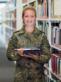 Eine Soldatin steht mit einem Tablet in der Hand in einer Bibliothek