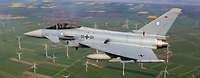 Kampfflugzeug Eurofighter fliegt über einen Windpark