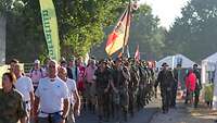 Eine Marschgruppe deutscher Soldaten in der Mitte ziviler Bevölkerung.