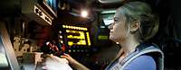 Erprobung MELLS Eine Frau sitzt in einem mit vielen elektronischen Geräten umgebenen Arbeitsplatz eines Fahrzeugs