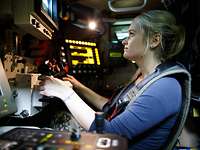 Eine Frau sitzt in einem mit vielen elektronischen Geräten umgebenen Arbeitsplatz eines Fahrzeugs