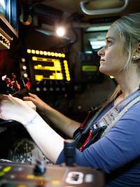 Erprobung MELLS Eine Frau sitzt in einem mit vielen elektronischen Geräten umgebenen Arbeitsplatz eines Fahrzeugs