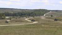Drei Panzer fahren über einen mit Gras bewachsenen Übungsplatz.