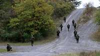 Eine Gruppe Soldaten bewegt sich in Schützenreihe auf eine Anhöhe zu.