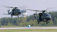 Zwei Hubschrauber der Bundeswehr schweben knapp über dem Boden über einer Landebahn