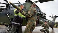 Zwei Soldaten bestücken einen Hubschrauber mit Munition.