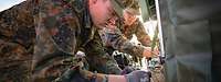 Zwei Soldaten sortieren kniend Daten- und Stromleitungen.