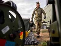 Ein Soldat hält eine Kabeltrommel in der linken Hand und lässt im Lauf Fernmeldekabel abrollen. 