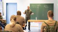 Österreichischer Offizier steht vor Deutschen Soldaten und unterrichtet. Auf der Tafel hinter ihm steht Covid-19 und Sars-Cov-2
