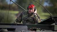 Ein Soldat schaut mit Kopfhörern mit Mikrofon aus einem Transportpanzer Fuchs heraus.