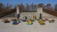 Frontalblick auf das Ehrenmal der Luftwaffe, an dem mehrere Kränze liegen und zwei Soldaten stehen.