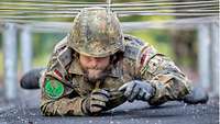 Mit Helm und Handschuhen unterkriecht ein Soldat gespannte Drähte.