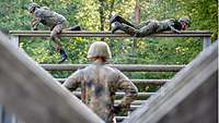 Zwei Soldaten überwinden ein hohes Gerüst aus Holz. 
