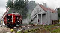 Ein Feuerlöschfahrzeug Gebäudebrand steht bei einer Übung vor einer Häuserattrappe aus der Rauch aufsteigt.