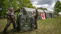 Vor einer Rettungsstation verladen zwei Soldaten Materialboxen.