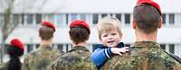 Betreuung und Fürsorge bei der Bundeswehr Ein Soldat hält seinen Sohn auf dem Arm, im Hintergrund angetretene Soldaten