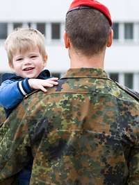 Betreuung und Fürsorge bei der Bundeswehr Ein Soldat hält seinen Sohn auf dem Arm, im Hintergrund angetretene Soldaten