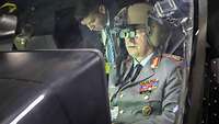 Ein General sitzt mit einem Pilotenhelm in einem Flugzeug.