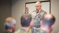 Ein General steht vor Soldaten und hält einen Vortrag. Dabei hebt er die rechte Hand halbhoch.