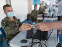 Ein Soldat mit Mundschutz sitzt an einem Computer und übergibt einer Person ein Corona-Teströrchen