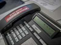Nicht für vertrauliche Informationen geeignet Ein Tastentelefon mit der Aufschrift am Hörer: "Do not discuss classified information".