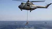 Der Helikopter im Schwebeflug über dem Flugdeck der Korvette. Das Boardingteam seilt sich ab