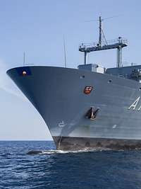 Ein graues Schiff von schräg vorne auf dem Meer bei Sonnenschein aus der Froschperspektive