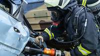 Ein Brandschützer bricht mit einem Rettungsspreizer die Tür eines Unfallwagens auf.