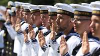 Marinesoldaten in Matrosenuniform, in Reihe angetreten, heben die Hand, um einen Eid zu schwören.