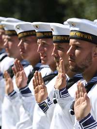 Marinesoldaten in Matrosenuniform, in Reihe angetreten, heben die Hand, um einen Eid zu schwören.