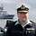 Rainer Brinkmann Ein Admiral in blauer Arbeitsuniform, im Hintergrund ein graues Kriegsschiff auf See