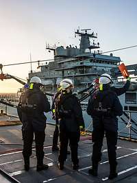 Auf dem Oberdeck eines Schiffes steht eine Gruppe von fünf Marinesoldaten in blauer Arbeitsuniform und mit Schutzhelmen.