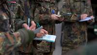 Aktuelles Mehrere Soldaten stehen mit Schreibblöcken und Stiften im Halbkreis und schreiben.